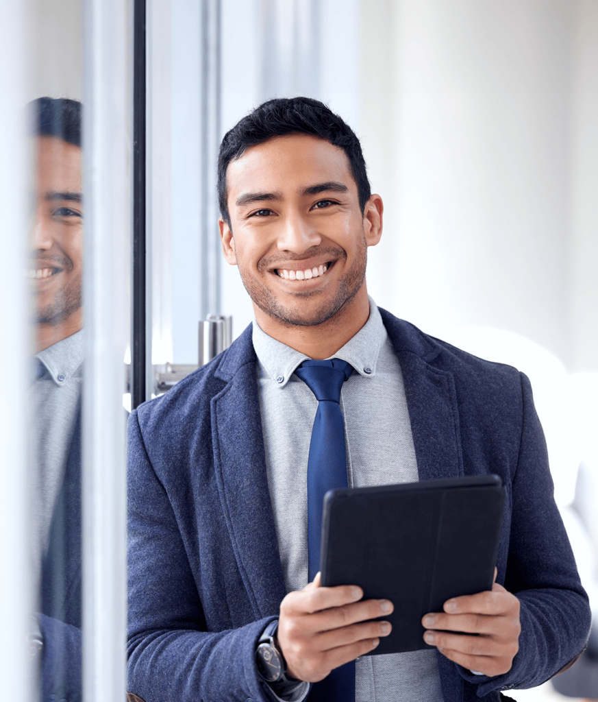 Jovem Empresário Sorridente Segurando um Tablet - G2B Contabilidade e Assessoria Financeira Jovem empresário sorridente, vestindo um terno azul marinho e gravata combinando, segurando um tablet em um ambiente corporativo moderno. Ele está posicionado ao lado de uma janela de vidro, que reflete sua imagem, criando um efeito visual agradável. Esta imagem é ideal para ilustrar a página de contato daG2B Contabilidade e Assessoria Financeira, destacando profissionalismo, acessibilidade e um atendimento amigável.